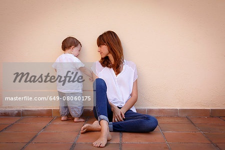 Mid adult woman with curious baby daughter on kitchen floor