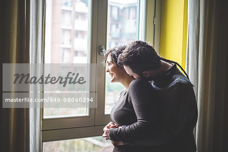 Couple standing by window, embracing