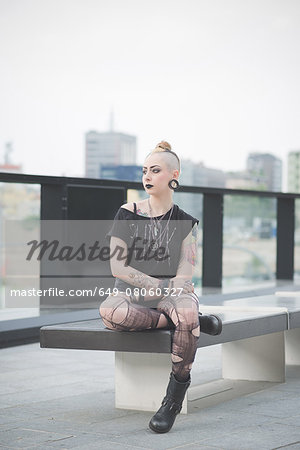 Portrait of young female tattooed punk sitting rooftop wall