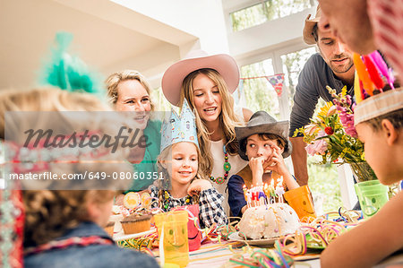 Three generation family at kids birthday party watching girl with birthday cake