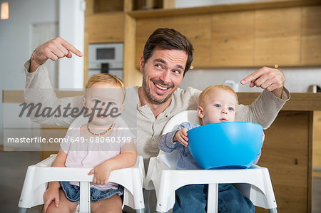 Father pointing at male and female twin toddlers in high chairs