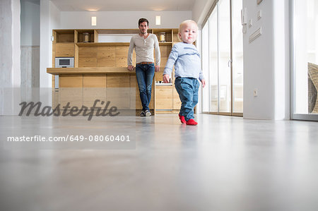 Father watching male toddlers walking on dining room floor