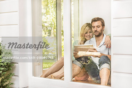 Mid adult couple sitting on floor using digital tablet at house window