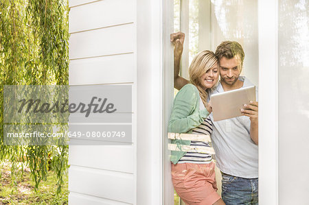 Mid adult couple using digital tablet at house window