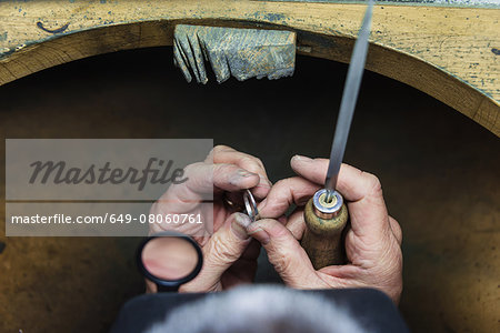 Hands of jewellery craftsman using file tool on platinum ring
