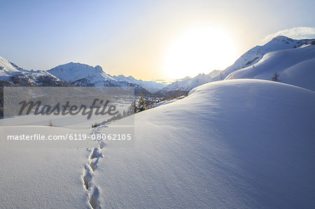 Footprints marching towards the Maloja Pass under a sun veiled by the mist on a cold winter day, Maloja, Graubunden, Switzerland, Europe