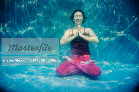 Mature woman wearing red yoga pants and vest, in yoga position, underwater view