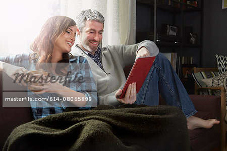 Young couple sitting on sofa drinking coffee and looking at digital tablet