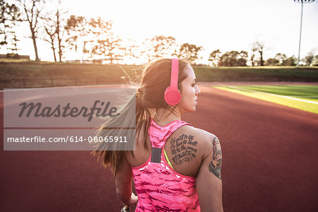 Rear view of young tattooed female athlete running on race track