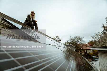 Portrait of mid adult woman sitting on newly solar paneled house roof