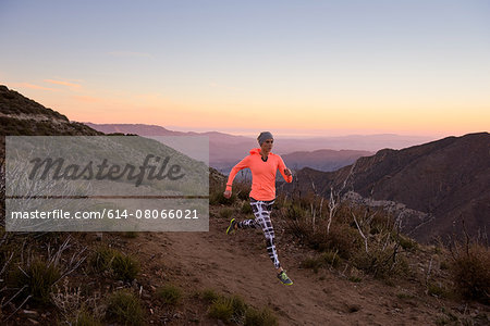 Rear view of young woman trail running down dirt track at dusk on Pacific Crest Trail, Pine Valley, California, USA