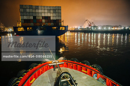 Tugboat manoeuvring cargo ship in harbor at night, Tacoma, Washington, USA