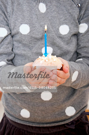 Child on birthday party holding cupcake with burning candle, Munich, Bavaria, Germany Child on birthday party holding cupcake with burning candle, Munich, Bavaria, Germany