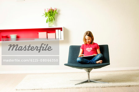 Girl sits in chair using tablet computer, Munich, Bavaria, Germany