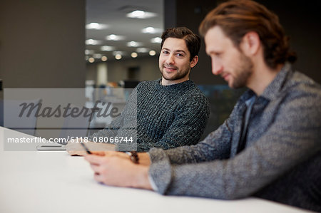 Two men seated at a table, one using his smart phone.