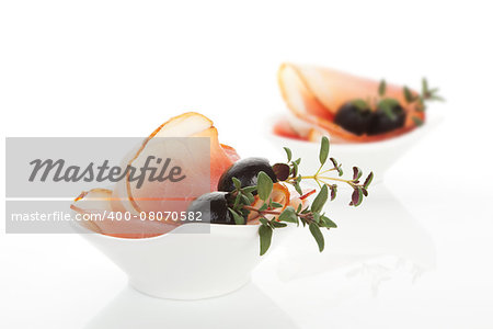 Culinary food. Prosciutto slices with black olives and fresh herbs in white bowl isolated on white background.