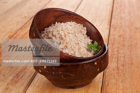 Sea salt flakes in wooden oriental bowl on wooden background with fresh herb. Natural salt background.
