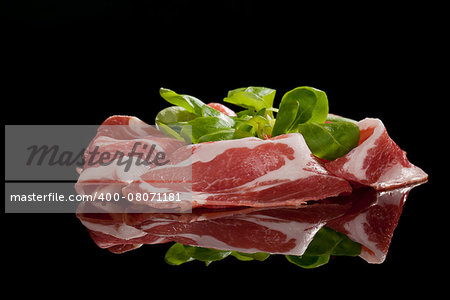 Delicious prosciutto slices with green corn salad isolated on black background. Culinary traditional italian ham.