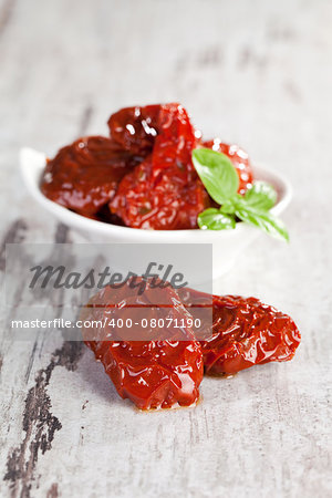 Dried tomatoes pomodoro with fresh basil leaves on white wooden textured background. Culinary traditional mediterranean eating.