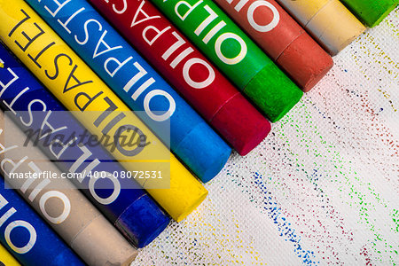 Many oil pastel crayons of different bright, vibrant and saturated colours, all lined up one next to the other on art paper, and viewed from up close.