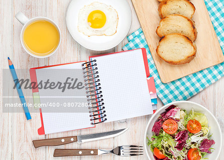 Healthy breakfast with fried egg, toasts and salad on white wooden table with notepad for copy space