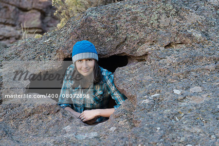 A young woman is casually posed and smiling from a large hole in a rock.