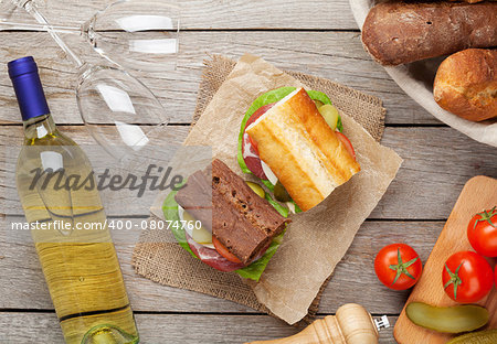 Two sandwiches with salad, ham, cheese and tomatoes with white wine on wooden table. Top view