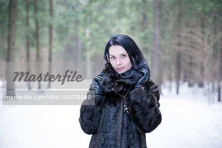 Brunette girl wearing a fur coat in winter forest