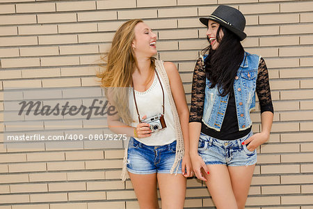 Two beautiful and young girlfriends having fun, in front of a brick wall