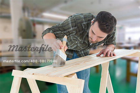 Worker using brush on wooden plank against workshop