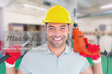 Happy repairman holding hammer and drill machine against workshop