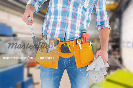 Midsection of handyman holding hammer and gloves against workshop