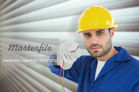 Confident repairman holding cables against grey shutters