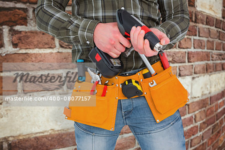 Manual worker holding gloves and hammer power drill  against red brick wall