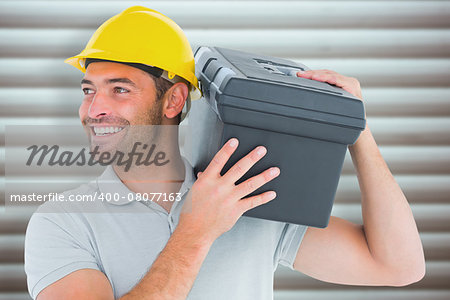 Handyman carrying toolbox on shoulder against grey shutters