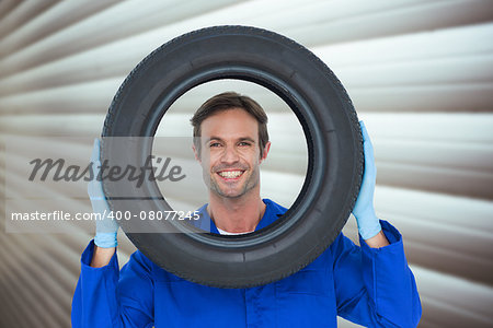 Confident mechanic looking through tire against grey shutters