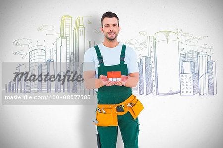 Happy construction worker holding house model against grey