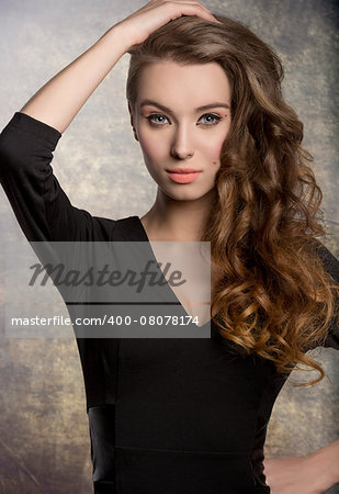 fashion brunette female posing with cute black dress, stylish make-up and long shiny wavy hair. Charming expression looking in camera