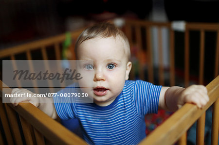 A 10 months baby boy standing in his playpen