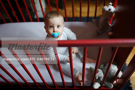 A 10 months baby boy sitting in his baby's cot