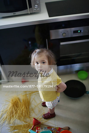 A 2 years old little girl posing in a kitchen in which she made the mess