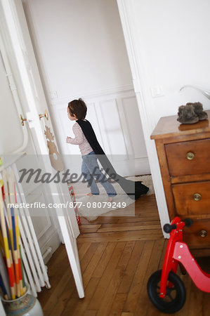 Little boy playing with a black cape, he runs in a hallway