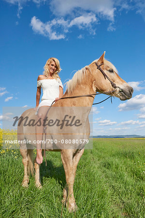 Portrait of young woman sitting on a Haflinger horse in a meadow in spring, Bavaria, Germany