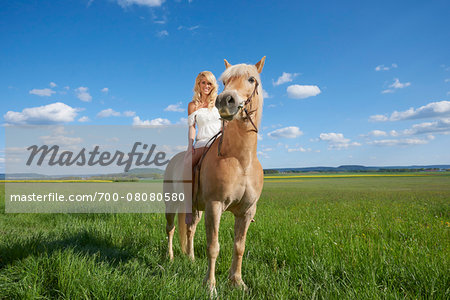 Portrait of young woman sitting on a Haflinger horse in a meadow in spring, Bavaria, Germany