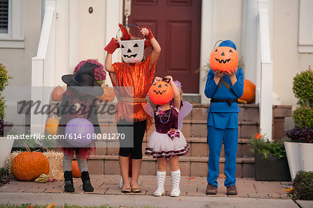 Children covering face with Jack O' Lantern bucket in front of house