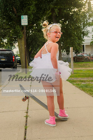 Young girl wearing tutu and pink baseball boots, standing on skateboard