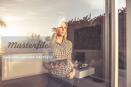 Portrait of young woman with digital tablet gazing from suburban window Portrait of young woman with digital tablet gazing from suburban window
