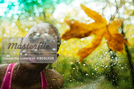 Portrait of young woman looking through rain covered window