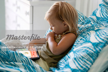Female toddler sitting up in bed using digital tablet