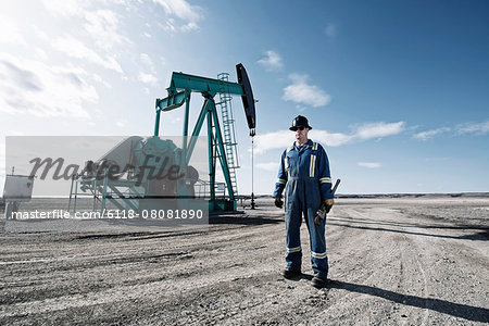 A man in overalls and a hard hat with a large wrench working at an oil extraction site. A man in overalls and a hard hat with a large wrench working at an oil extraction site.